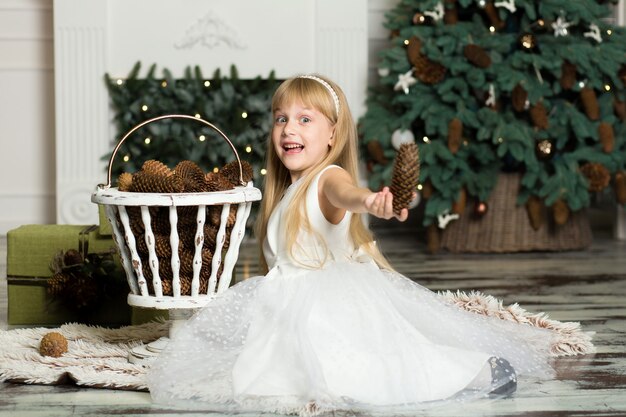 Little girl in a white dress plays with pine cones