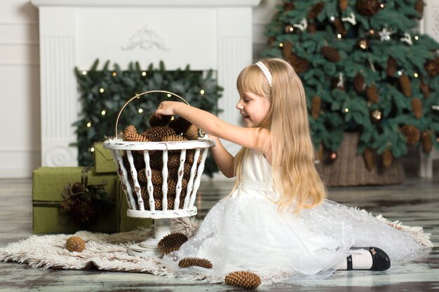 La bambina in un vestito bianco gioca con le pigne