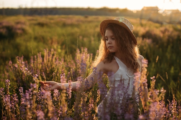 夏の野原に美しい花を持つ白いドレスを着た少女