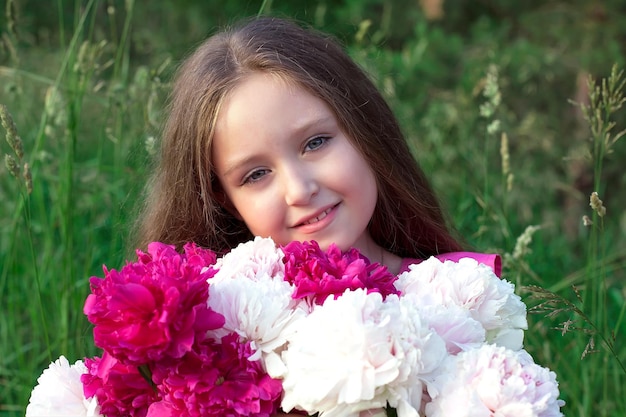 A little girl in a white dress with a bouquet of pink peonies on a blurry green background Photo shoots in nature