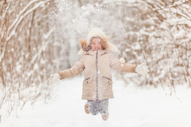 Little girl in a white hat and jacket in the winter forest throws snow. Winter fun