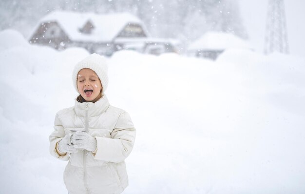 白いジャケットと白い帽子をかぶった少女が、美しい雪の吹きだまりと森を背景に、降雪時にお茶を片手に持っています。