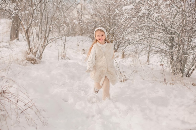 a little girl in a white knitted hat and sweater runs around a snowy park