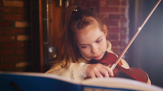 A little girl in white sweater playing violin by notes