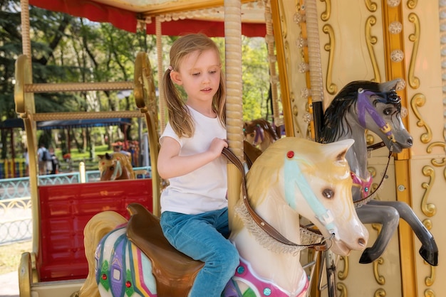 Little girl in a white tshirt rides a carousel in an amusement park copy space