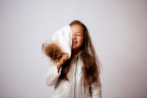 Bambina in cappello di inverno che sorride sul bianco