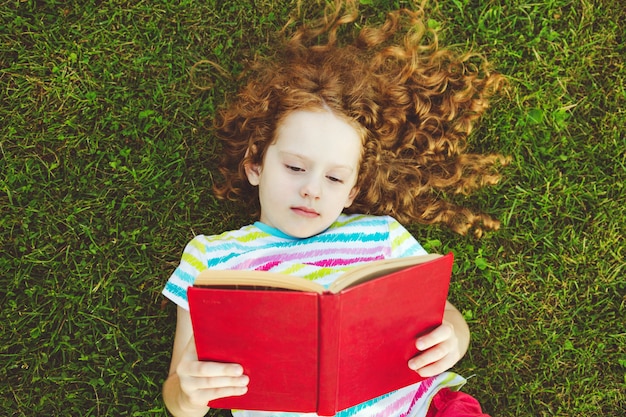Фото Маленькая девочка с книгой, лежащий в траве.