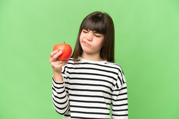 Little girl with an apple over isolated chroma key background with sad expression