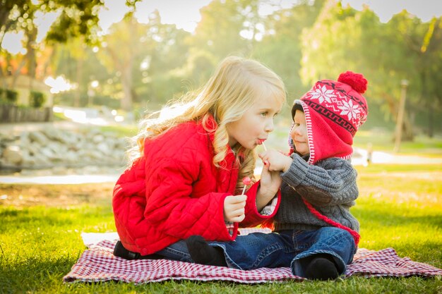 Маленькая девочка с маленьким братом в пальто и шляпах на открытом воздухе