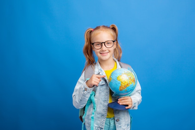 A little girl with a backpack holds a globe on a blue background