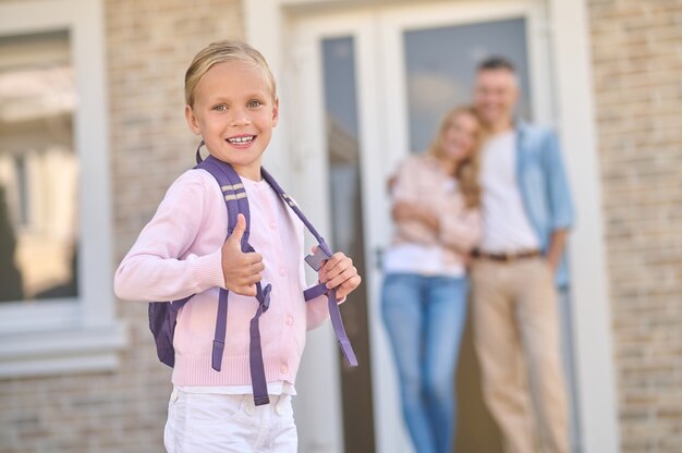 Little girl with backpack showing ok and parents