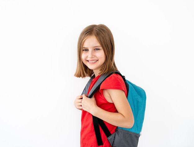 Little girl with backpack standing sideways isolated on white