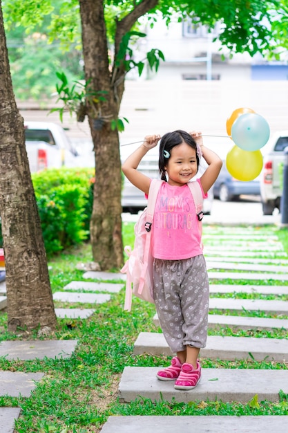 Little girl with balloon and backpack walking in the park