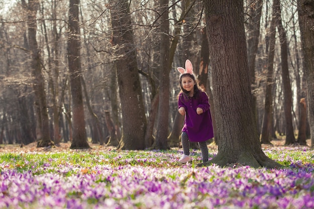 Little girl with banny ears peeping from behind a tree in the park