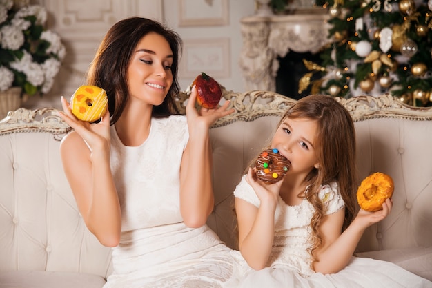 Bambina con bella madre divertirsi con le ciambelle