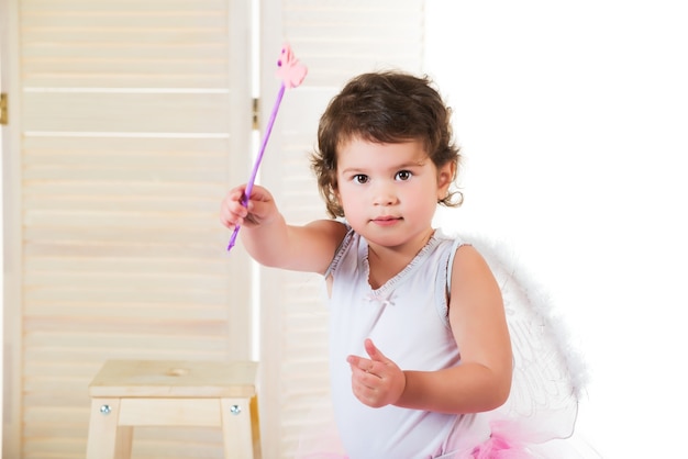 Little girl with big brown eyes, dressed in fairy costume, hand raised up and holds magic wand