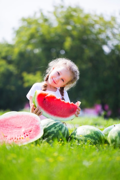 Маленькая девочка с большим арбузом ломтик в летнее время в парке. Ребенок, здоровое питание.