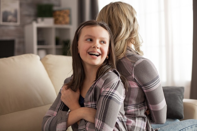 Bambina con un grande sorriso e bretelle seduta schiena contro schiena con sua madre sconvolta su di lei. ragazzo disobbediente