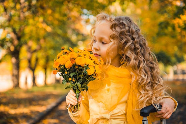 Little girl with blond hair in autumn background with flowers and suitcase