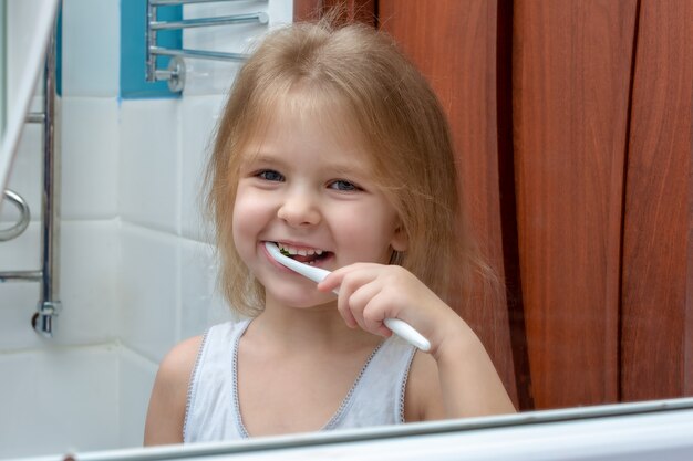 A little girl with blond hair brushing her teeth.