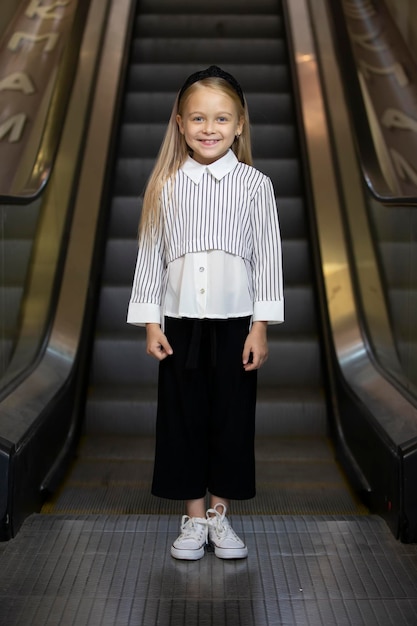 A little girl with blond hair stands at the subway excalator