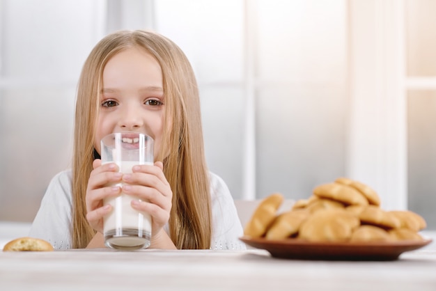 Маленькая девочка со светлыми волосами пьет стакан с молоком