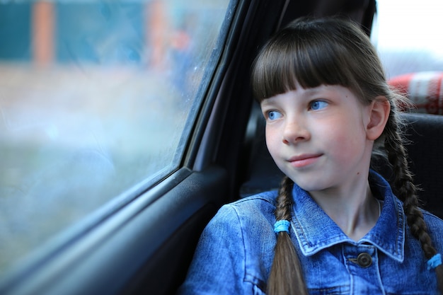 窓で車の後ろに座っている青い目を持つ少女