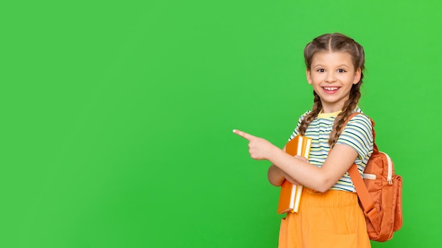 A little girl with books and a briefcase points to an advertisement. Isolated background.