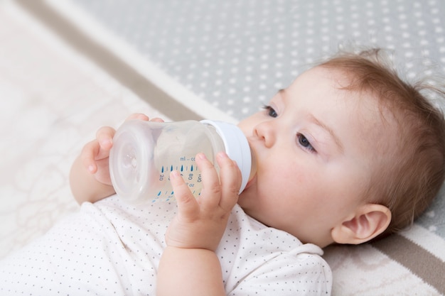 Little girl with a bottle in her hands and a pacifier in her mouth