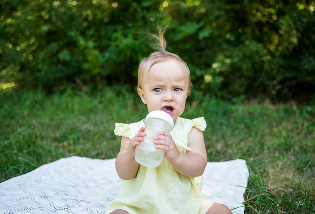 A little girl with a bottle of water sitting on a blanket in nature