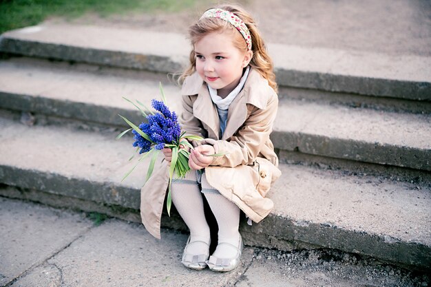 маленькая девочка с букетом синих цветов сидит на лестнице