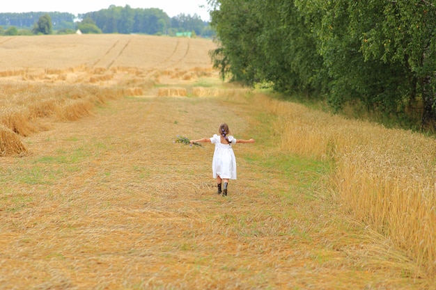 Little girl with a bouquet of wildflowers in her hands in a wheat field.