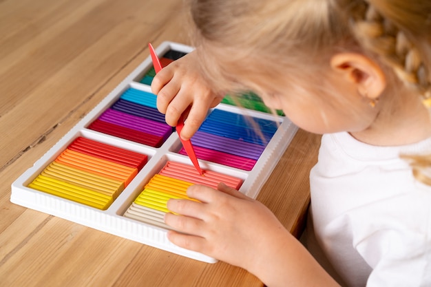 A little girl with a bright colorful palette of colored plasticine for modeling hobbies