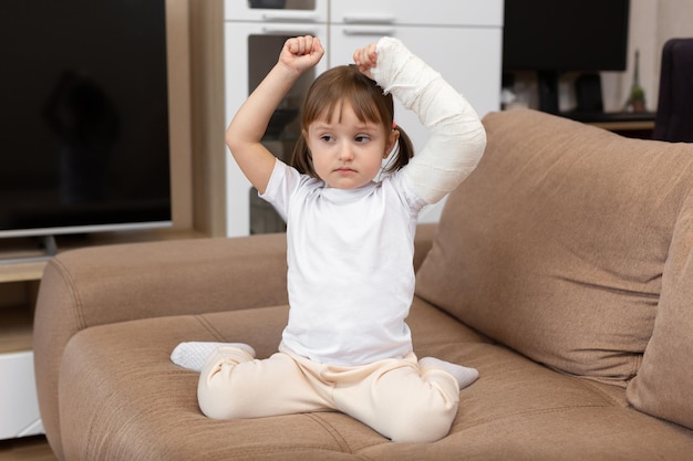 A little girl with a broken arm and a cast raises her arms\
up