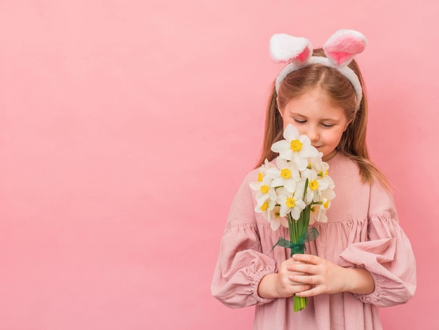 Photo little girl with bunny ears smelling narcissus flowers over pink background