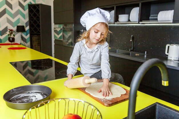 Little girl with chef hat rolling pin preparing dough bake homemade holiday apple pie in kitchen kid