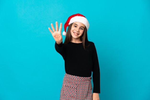 Bambina con cappello di natale isolato su sfondo blu felice e contando quattro con le dita