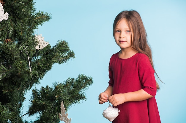 파란 벽에 크리스마스 나무를 가진 어린 소녀입니다.