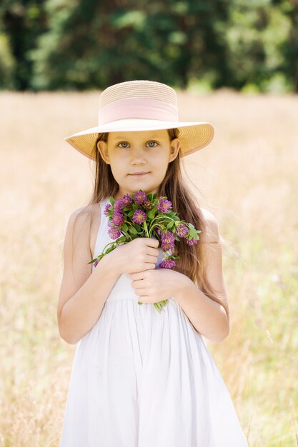 牧草地の帽子にクローバーの花束を持つ少女