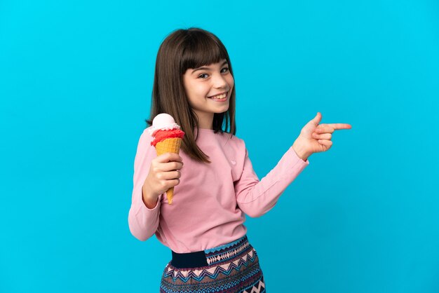 Little girl with a cornet ice cream isolated on blue background pointing finger to the side