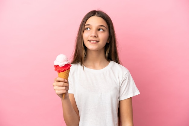 Little girl with a cornet ice cream over isolated pink background thinking an idea while looking up