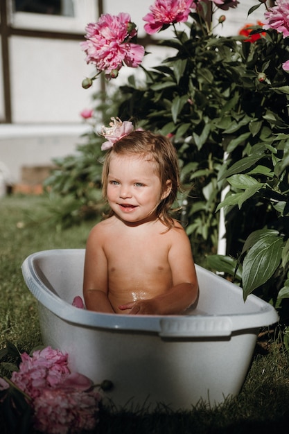 Photo a little girl with a crown on her head is bathing in a small bath with peonies