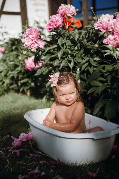 머리에 왕관을 쓴 어린 소녀가 모란이 있는 작은 욕조에서 목욕하고 있다