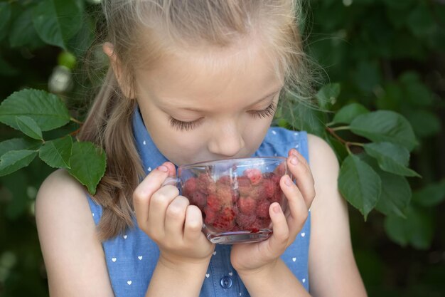 庭にラズベリーを持った女の子 健康的な自然栄養
