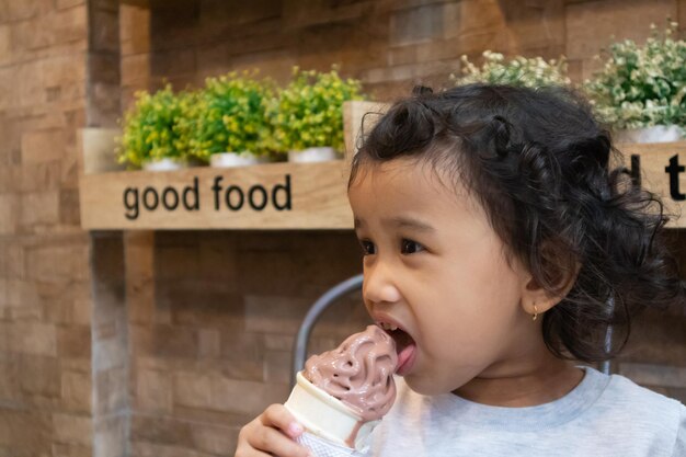 A little girl with curly hair eating a chocolate ice cream in the cafe