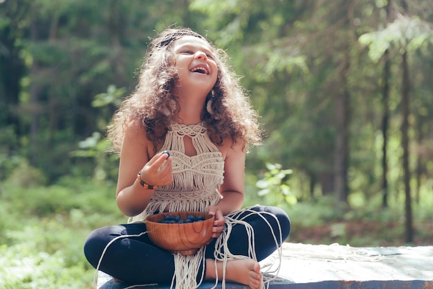 Photo a little girl with dark curly hair dressed as a native in the forest eats berries