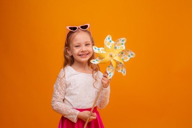 a little girl with dark glasses holds a toy windmill on a yellow background