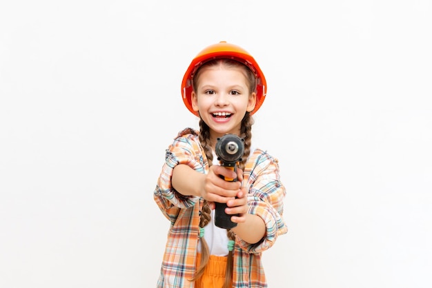 A little girl with a drill and wearing a protective construction helmet depicts a builder on a white isolated background The concept of repair