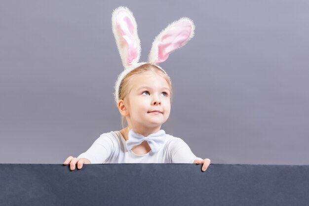 A little girl with ears from a white rabbit suit, will hold a sheet of black cardboard.