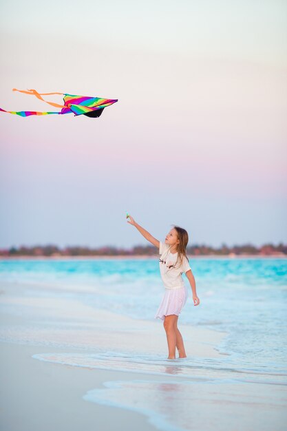 Little girl with flying kite on tropical beach.